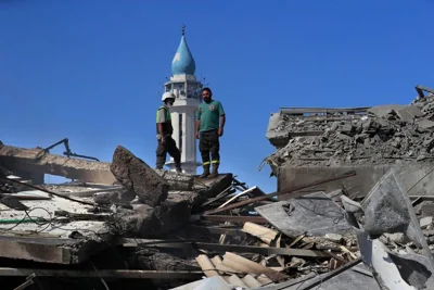 A Hezbollah rescue worker, left, and a Lebanese Civil Defence worker, right, stand on the rubble of destroyed buildings at commercial street that was hit Saturday night by Israeli airstrikes, in NAbatiyeh town, south Lebanon, Sunday, Oct. 13, 2024. (AP Photo/Mohammed Zaatari)