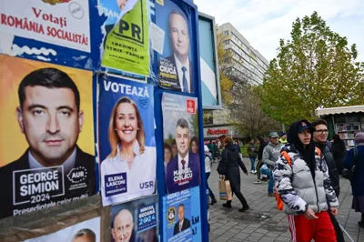 People pass by electoral posters with candidates for the presidential and parliamentary elections in Bucharest on November 22, 2024. [Daniel Mihailescu / AFP]