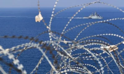 Navy vessel seen through a closeup of a tangle of barbed wire