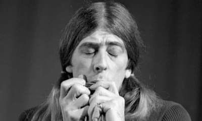 Man with long hair plays harmonica in black and white photo