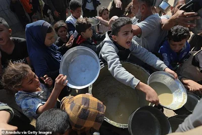 Palestinians in a densely packed crowd hold metal pots and pans as they attempt to reach for food being distributed amid Israeli attacks in Deir al-Balah, Gaza on November 23