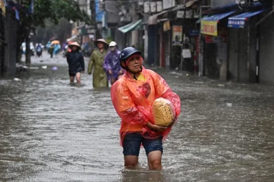 A woman carries a bag of rice through flood waters on a street in Hanoi