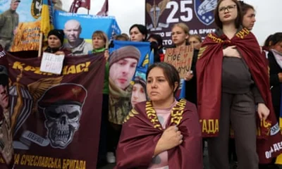 A group of women stand and sit holding banners, placards and pictures of the missing soldiers