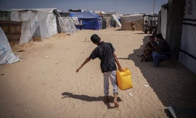 A boy carries a large bottle of water past tents in Rafah