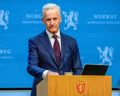A man in a dark blue suit at a lectern in front of a blue backdrop that reads “Norway.”