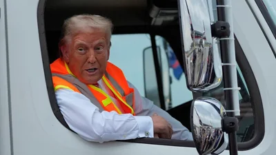 Donald Trump in garbage truck passenger seat in orange vest