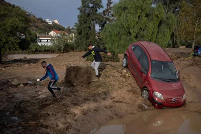 Men run next to a car covered with mud on a flooded street in Alora, near Malaga, on October 29, 2024, after a heavy rain hit southern Spain. AFP PHOTO