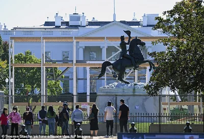 Passers-by stand in front of a fence on the grounds of the White House