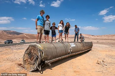 eople stand on top of the remains of an Iranian missile in the Negev desert near Arad, on October 2