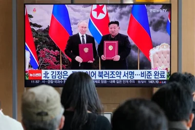 The backs of heads of people are seen as they watch a television screen with two men standing in front of flags.