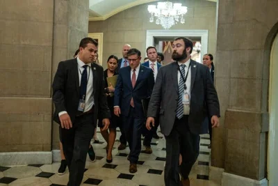 Mike Johnson, center, walks amid several other people in a room with a chandelier.