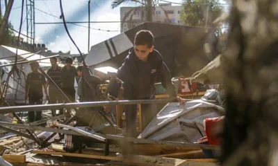 Child among rubble with adults in background