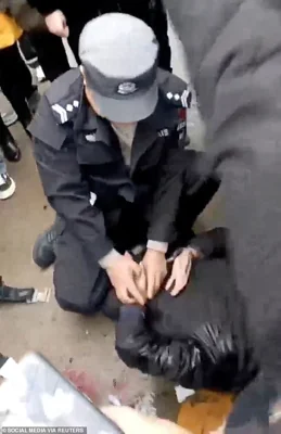 A police officer handcuffs a man on the ground following a vehicle collision outside a primary school in Changde