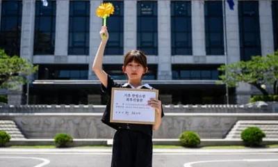 Jeah Han stands outside the constitutional court in Seoul while holding her closing argument in one hand. She is also holding aloft a yellow paper flower