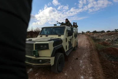 Fighters from Hayat Tahrir al-Sham (HTS) ride in military vehicles in the eastern outskirts of the town of Atarib, in Syria's northern province of Aleppo on November 27, 2024, during clashes with the Syrian army. - At least 57 people were killed in clashes sparked by a surprise jihadist attack on the Syrian army, a war monitor said. (Photo by Abdulaziz KETAZ / AFP)