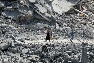 Palestinians walk past debris from previous Israeli bombardments, in Khan Yunis on July 4