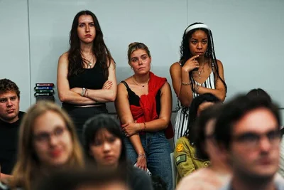 College students, some standing and some seated, look forward with straight expressions on their faces.