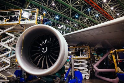 The interior of an aircraft factory, with a jet engine prominent in the foreground.