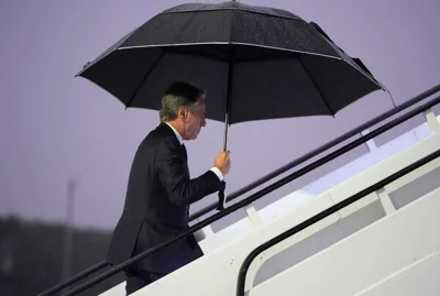 Antony Blinken carries a black umbrella as he walks up steps to a plane.