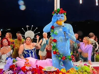 A performer painted blue and covered in flowers and fruit, depicting the Greek god Dionysus, sang in French