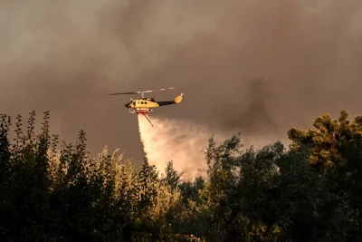 A helicopter drops a load of water over houses during a wildfire in Varnavas, north of Athens, on August 11, 2024. AFP PHOTO