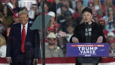 Republican presidential nominee former President Donald Trump listens as Elon Musk speaks during a campaign rally at the Butler Farm Show, Saturday, Oct. 5, 2024, in Butler, P