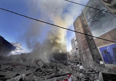 Smoke rises near a portrait of the late Hezbollah military commander Imad Mughniyeh from a destroyed building hit by an Israeli air strike in Beirut, 20 October, 2024