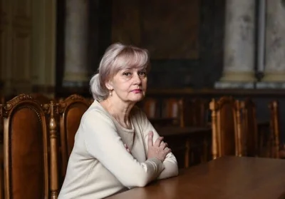 Iryna Farion sits at a wooden table in a grand room with her arms folded.