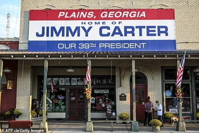 A local resident of Plains and friend of former US President Jimmy Carter Gloria English (R), along with her care taker Stacy Ludden, walk beneath a sign reading 'Home of Jimmy Carter' in Plains, Georgia, on September 30, 2024, ahead of his 100th birthday