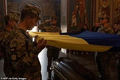 Ukrainian soldiers hold a national flag over the coffin of Ukrainian serviceman Ruslan Troianchuk, callsigned "Friend", who was killed in the Donetsk region