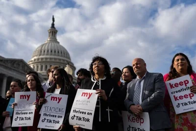 A group of people holding signs in support of TikTok stand against a backdrop of the U.S. Capitol and dramatic clouds.