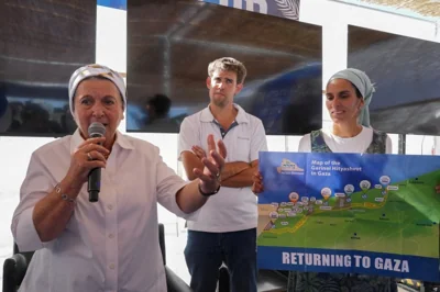 a woman wearing white speaks as another woman holds.a poster with a map of gaza