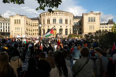 A crowd of people, one with a large Palestinian flag, in front of a stately building.