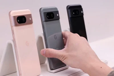 A hand reaches out to three differently colored smartphones.