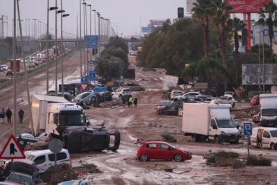 People walk by cars and trucks that were among the debris swept up in recent flash flooding