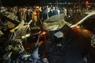 People stand near the wreckage of vehicles as they gather after an explosion near Jinnah International Airport in Karachi