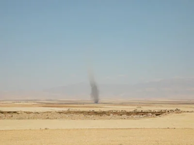 A column of black smoke rises in the middle of an empty field. 