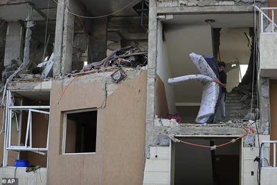 A man carries mattresses from a destroyed building hit by an Israeli airstrike, in Barja village