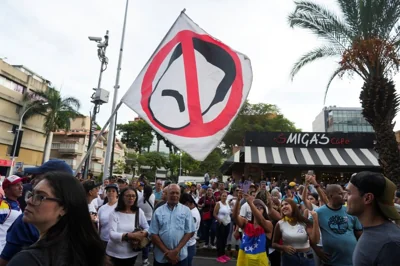 A protester in a crowd holds up a flag that shows a cartoon of Nicolas Maduro's mustachioed face crossed out.