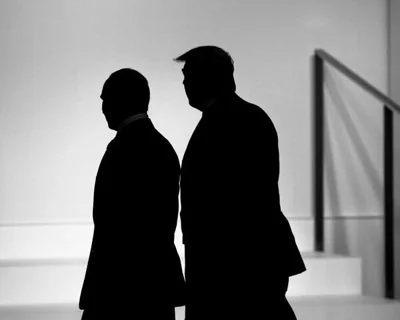 Vladimir Putin and Donald Trump standing alongside each other, cast in shadow. 