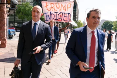 Emil Bove and Todd Blanche leave the US Federal Courthouse in Washington, DC, as protesters behind them celebrate Trump's indictment.