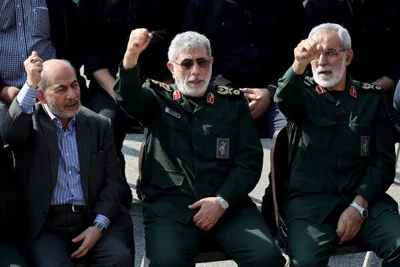 Three people, two in military uniform, are seated together and hold their fists in the air.