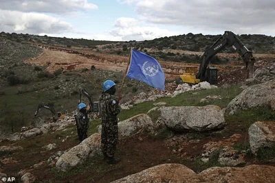 UN peacekeepers hold their flag, as they observe Israeli excavators attempt to destroy tunnels built by Hezbollah in 2019