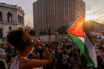 A group of protesters hold signs and a large Palestinian flag at an intersection in Harlem.