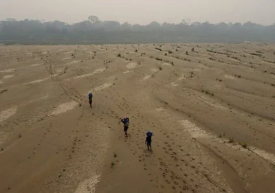 An aerial photo shows three people walking across a dry, sandy riverbed. 