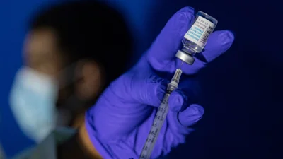 A hand in a blue rubber glove draws a vaccine into a syringe.