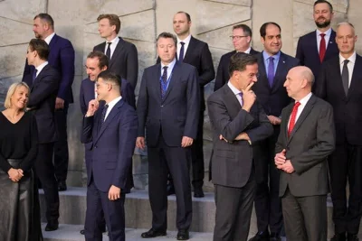 A group of men and one woman, all dressed in business attire, chat as they wait for a picture to be taken.