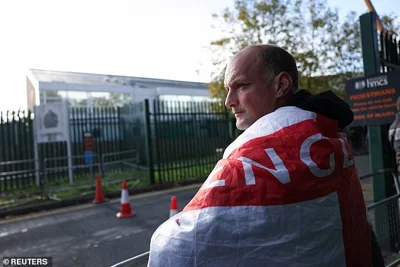 A man wearing an English flag looks on as supporters of Robinson gather outside Woolwich Crown Court