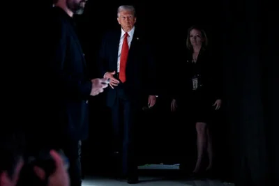 President Trump, in a red tie, stands against a dark backdrop.