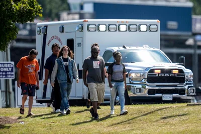 Students walk away from Apalachee High School as an ambulance responds to the school. The 14-year-old suspected gunman is alive and in custody and police plan to charge him as an adult